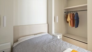A modern bedroom with a bed, nightstands, a wardrobe, and a hanging rack with clothes. - Hoppersgr- Amazing apt in the heart of Athens - 1
 (Athina)