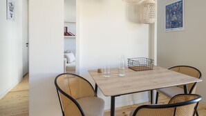 A dining area with a wooden table, four wicker chairs, and two hanging light fixtures. - Hoppersgr- Amazing apt in the heart of Athens - 1
 (Athina)