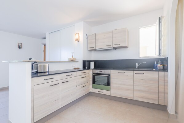 A modern kitchen with light wood cabinets, a black countertop, and a built-in oven.