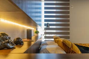 Una habitación moderna con una cama, una mesita de noche con objetos decorativos y una ventana con persianas.