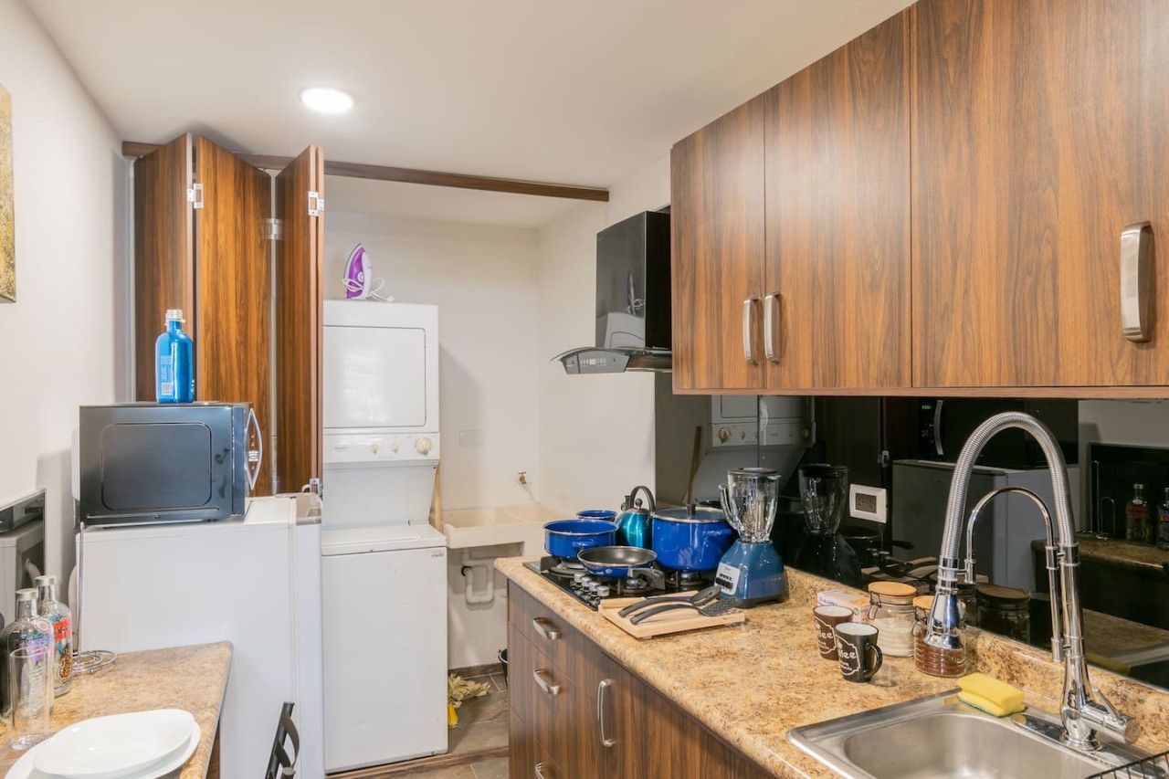 A compact kitchen with wooden cabinets, a microwave, a refrigerator, and a sink.