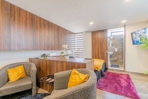 Un salon moderne avec un mur d’accent en bois, une table centrale en bois, deux canapés gris agrémentés de coussins jaunes et un tapis rose.