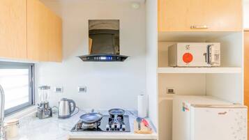 A compact kitchen with a stove, kettle, and a microwave on the countertop.
