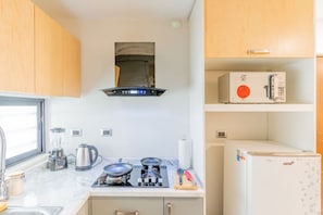 A compact kitchen with a stove, kettle, and a microwave on the countertop.