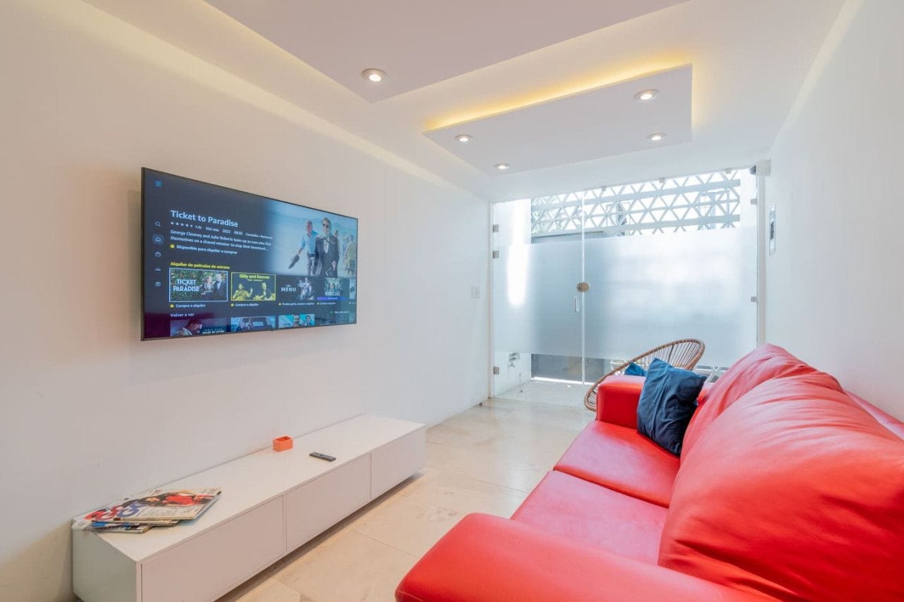Una sala de estar moderna con un televisor de pantalla plana montado en la pared, un sofá rojo y una consola blanca.