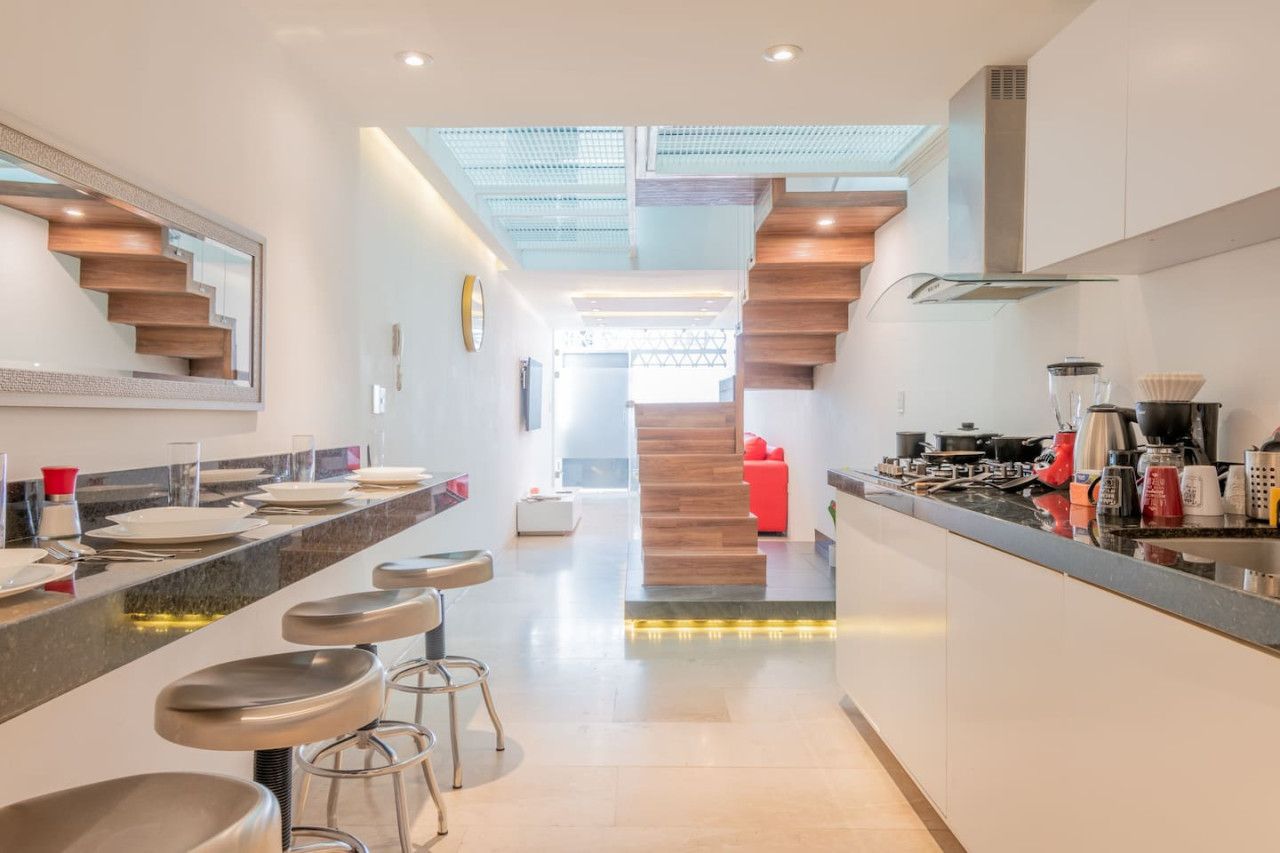 A modern kitchen with a central island, bar stools, and a staircase leading to an upper level.