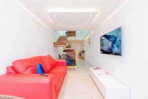 A modern living room with a red sofa, a flat-screen TV, and a staircase leading to an upper level.