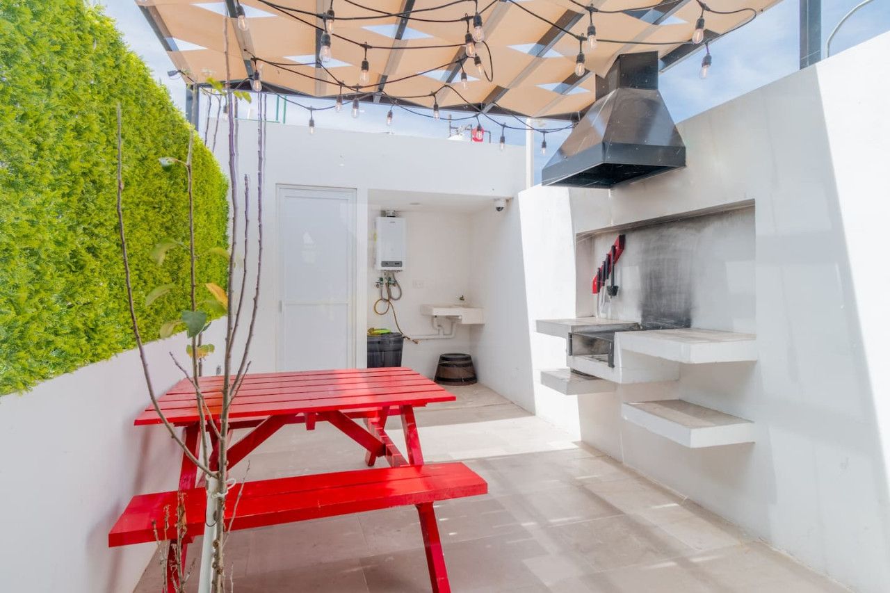 Un área de cocina al aire libre compacta con una mesa roja, una parrilla integrada y una pared verde.