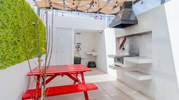Un área de cocina al aire libre compacta con una mesa roja, una parrilla integrada y una pared verde.