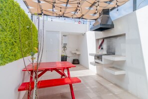 A compact outdoor kitchen area with a red table, a built-in grill, and a green wall.