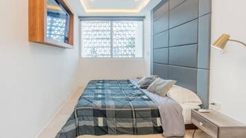 A bedroom with a bed, bedside table, lamp, and window with a geometric pattern.