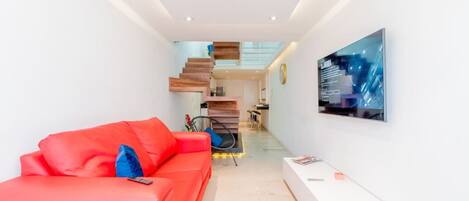 A modern living room with a red sofa, a flat-screen TV mounted on the wall, and a staircase leading to an upper level.