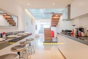 A modern kitchen with a central island, bar stools, a staircase, and a skylight.