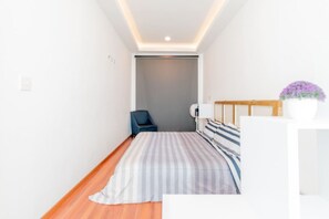 A narrow room with a bed, a chair, and a small table. - LOFT ULTRA Moderno y Minimalista | Cama KING Size (Durango)