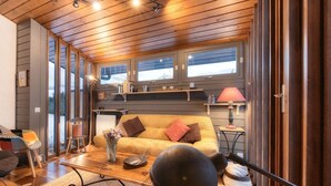 Een gezellige woonkamer met houten plafond, een bank met kussens, een salontafel en een lamp.