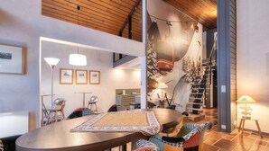 Een moderne eetruimte met een houten tafel, kleurrijke stoelen en een wanddecoratie met ski-thema.