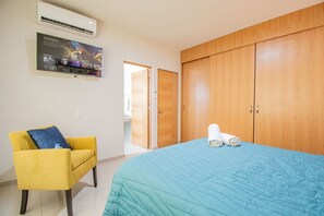 A bedroom with a bed, a chair, a wardrobe, and an air conditioning unit.
