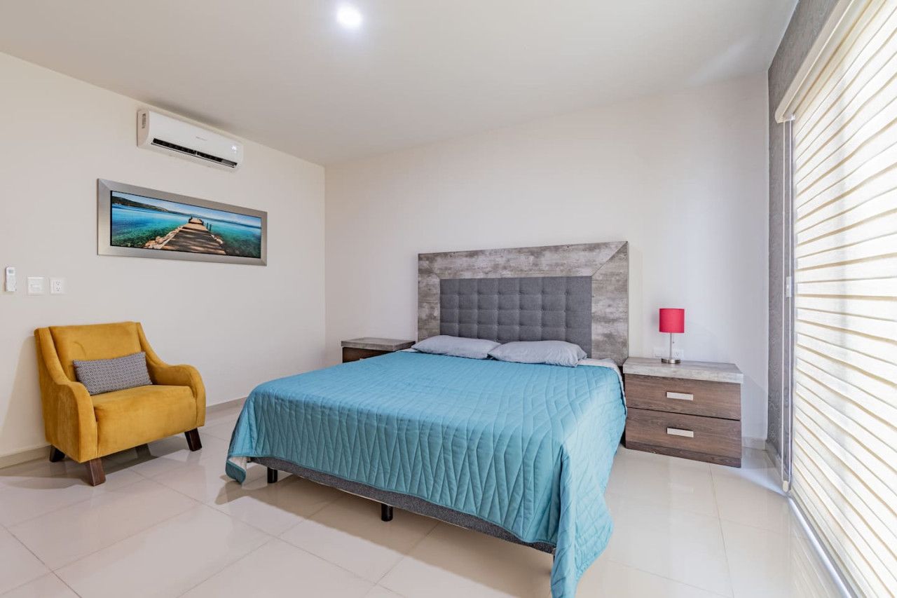 A bedroom with a bed, a nightstand, a chair, a picture on the wall, and a window with blinds.