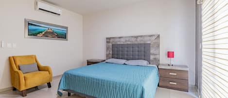 Ein Schlafzimmer mit einem Bett, einem Nachttisch, einem Sessel, einem Bild an der Wand und einem Fenster mit Jalousien.