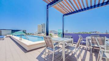 A rooftop terrace with a pool, outdoor seating, and a view of the city skyline.