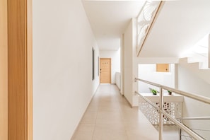 A modern hallway with a wooden door, a staircase with a railing, and a small plant on the landing.