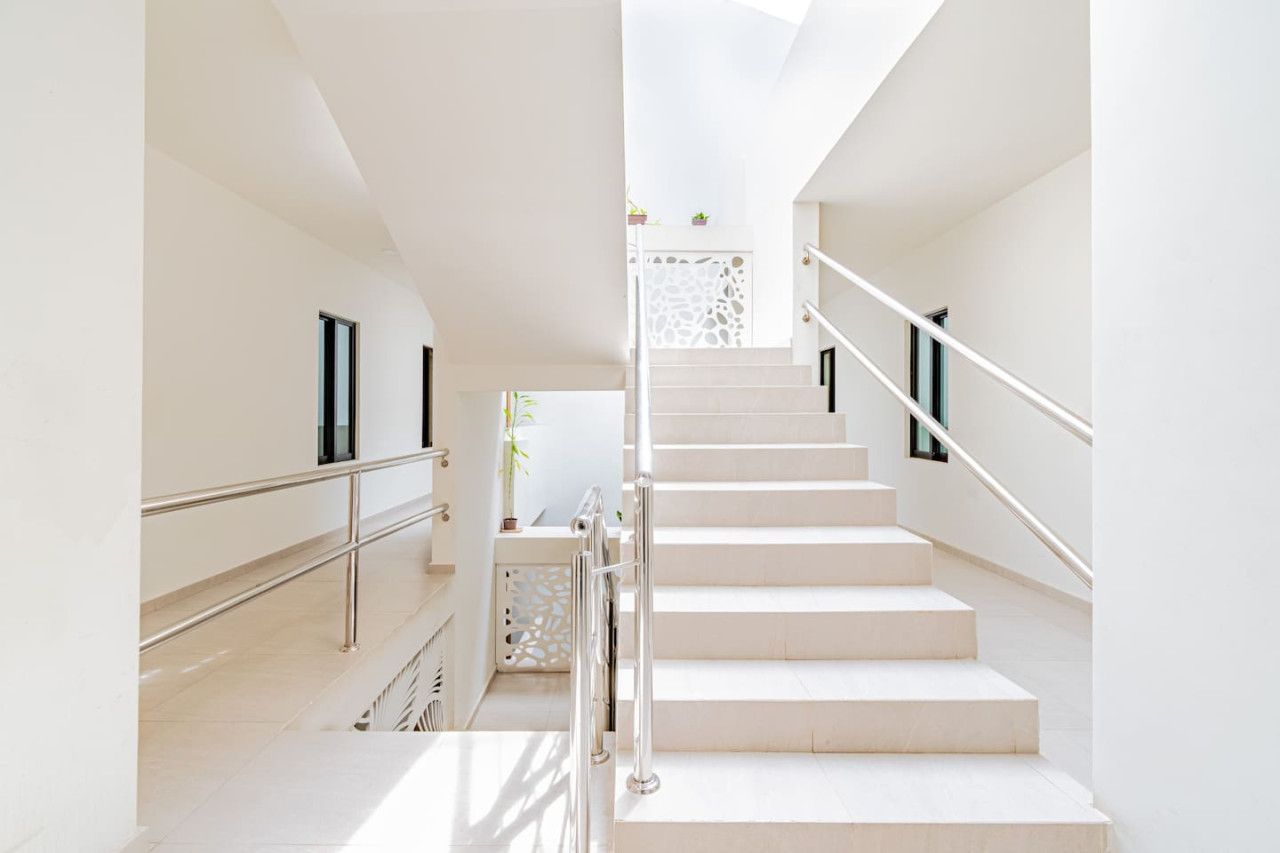 A modern staircase with a metal railing, leading to a landing with a decorative wall and a small plant.