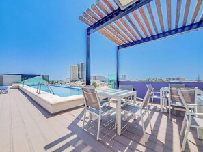 En pool på taget med udsigt over byens skyline, udendørs møbler og en pergola.