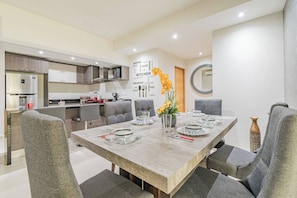 A modern kitchen with a dining area, featuring a wooden table set for four, grey upholstered chairs, and a decorative wall with food-related words. - Lujoso Condominio Tiburon a 3 Cuadras de la Playa (Mazatlán)