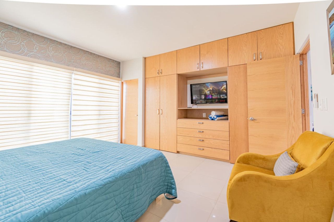 A bedroom with a bed, a television on a stand, wooden wardrobes, and a yellow armchair.