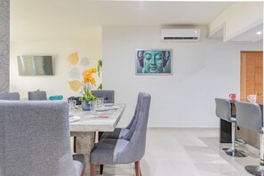A dining area with a table set for four, grey upholstered chairs, a vase with yellow flowers, and a framed artwork on the wall.