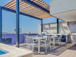 En tagterrasse med pool, udendørs møbler og udsigt over byen.