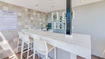A modern kitchen with a marble countertop, white bar stools, and a tiled backsplash.