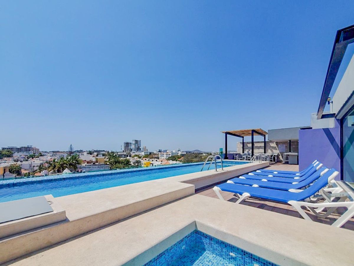 Una piscina en la azotea con sillones de descanso y vistas a la ciudad.