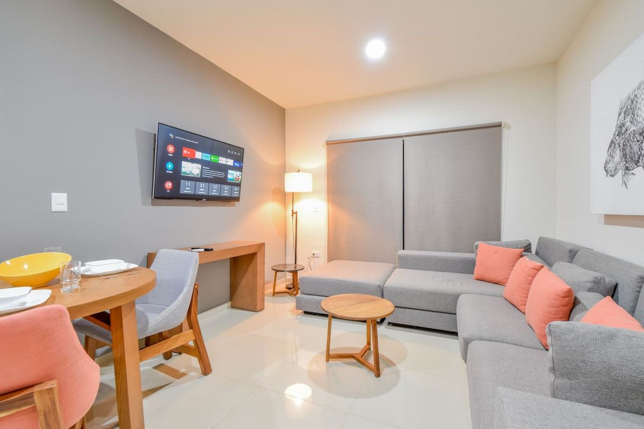 Ein modernes Wohnzimmer mit einem Flachbildfernseher, einem Sofa, einem Esstisch mit Stühlen und einer Lampe.