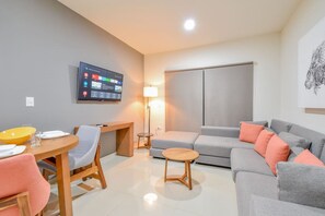 Una sala moderna con un televisor de pantalla plana, un sofá, una mesa de comedor con sillas y una lámpara.