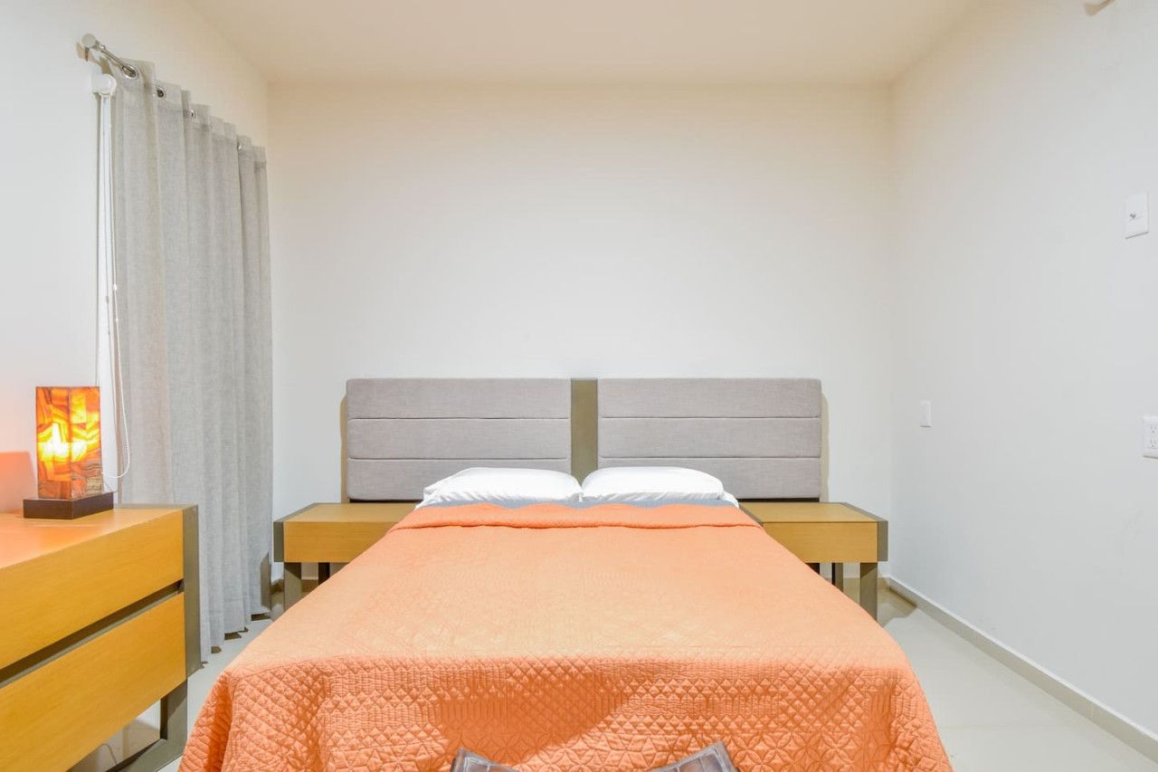 Una cama individual con cabecera, una mesita de noche con lámpara y una cortina.