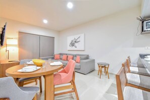 A modern living room with a sofa, dining table, and chairs, a TV mounted on the wall, and a painting above the sofa.