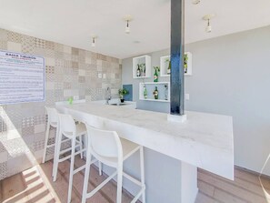 A modern kitchen with a marble countertop, white bar stools, and a patterned backsplash.