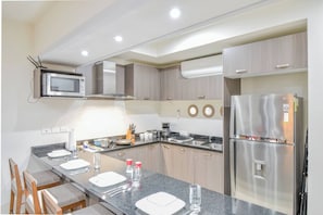 A modern kitchen with a microwave, stove, refrigerator, and a long counter with chairs.