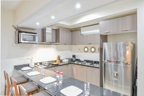 A modern kitchen with a built-in microwave, stainless steel refrigerator, and a long countertop with a sink.