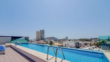 A rooftop pool with clear blue water, a cityscape view, and a modern building in the background.