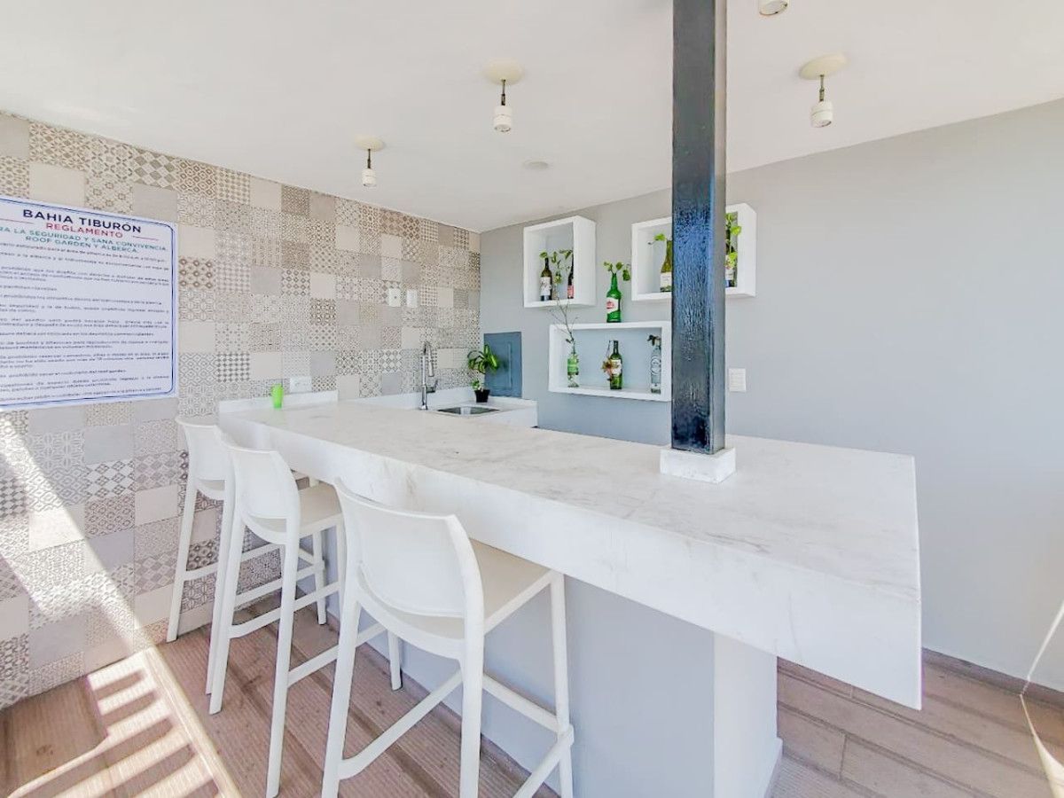 Una cocina moderna con encimera de mármol, sillas blancas y salpicadero con azulejos estampados.