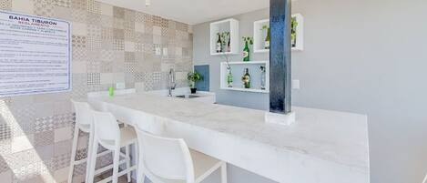 Una cocina moderna con encimera de mármol, sillas blancas y salpicadero con azulejos estampados.