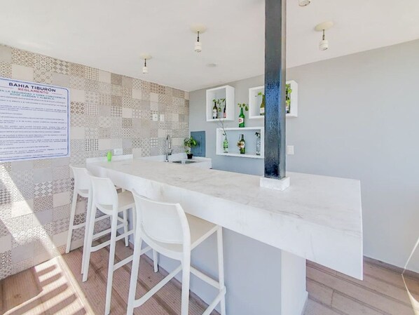 Una cocina moderna con encimera de mármol, sillas blancas y salpicadero con azulejos estampados.
