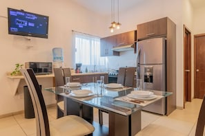 A modern kitchen with a dining area, stainless steel appliances, and a flat-screen TV.