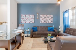 A modern living room with a brown sofa, a glass coffee table, and a dining area with a glass table and chairs.