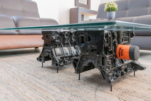 Un motor de coche sobre una mesa de cristal con una pequeña planta en maceta al fondo.