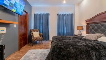 A hotel room with a bed, a chair, a TV mounted on the wall, and curtains on the windows.