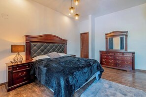 A bedroom with a bed, dresser, nightstand, lamp, and mirror.