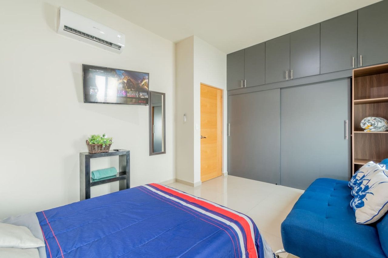 A bedroom with a bed, a wardrobe, a television, and a small table with a plant.